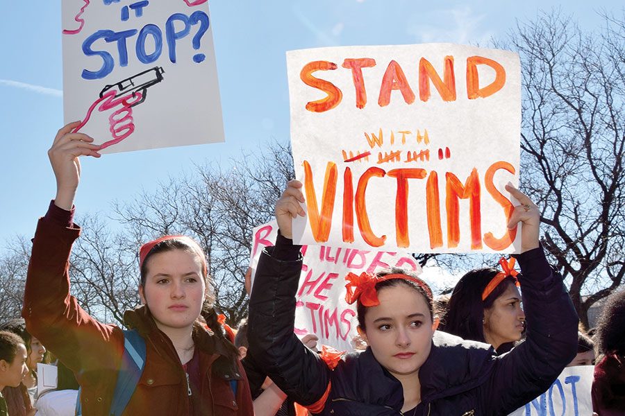 SIGNS OF SUPPORT. Raising both voices and posters, seniors Elena Sparrow and Alicia Haydon walk out for gun control and solidarity with victims of gun violence March 2. The day before, art teacher Sunny Neater-DuBow made available supplies and her classroom to people designing posters.
