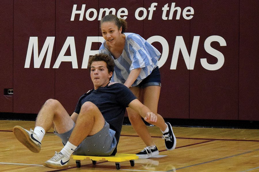 FIRST DAY FUN. Senior Connor Smith and sophomore Madeline Kolb participate in the annual scooter race at the first day assembly on Sept. 4. Students from different grades partnered together and pushed each other across the room in scooters. At the assembly, the new student council introduced themselves and stressed the importance of friendship between grades. 