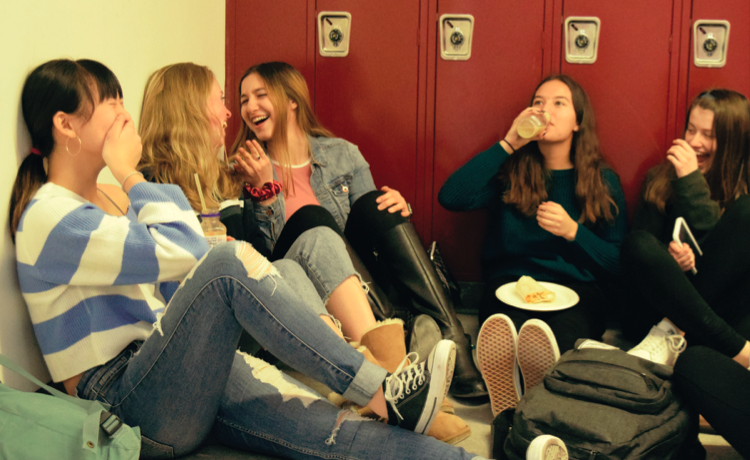 CONNECTING WITH FRIENDS. A group of ninth-grade students laugh between bits of their lunch in the freshman hallway earlier this year. This is only one of the many groups you can see if you walk through any hallway of the school during the lunch period. It has been increasingly clear that the cafeteria is not always the desired location to eat for many students through all of the grades.