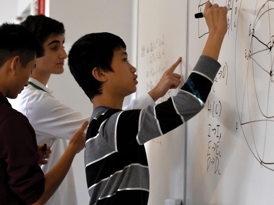 FINDING THE FORMULA: Surrounded by collaborating Mathematics team members, freshman Jeffery Chen works through questions on the white board. He said he enjoys coming up with creative solutions to difficult  locgic problems.