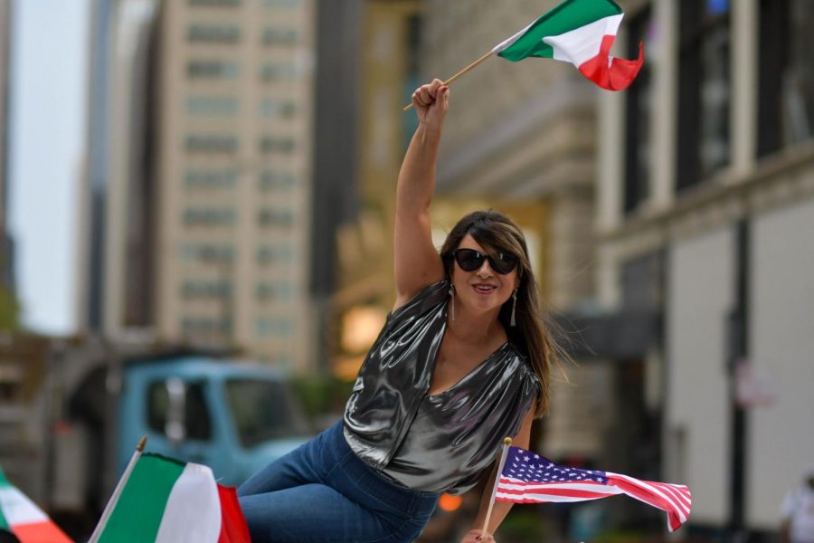 Waving an Italian flag and blowing kisses, a woman leans out of one an Italian car being showcased at the parade. 