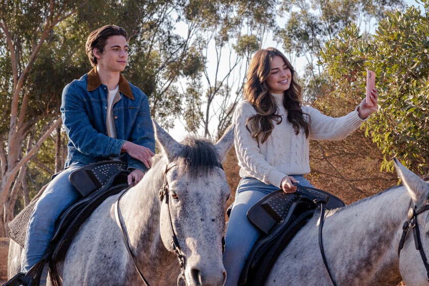 The lead characters Cameron Kweller (Tanner Buchanan) and Padgett Sawyer (Addison Rae) in “He’s All That” share a horseback ride through a mountain as Padgett live streams the ride to her followers. 