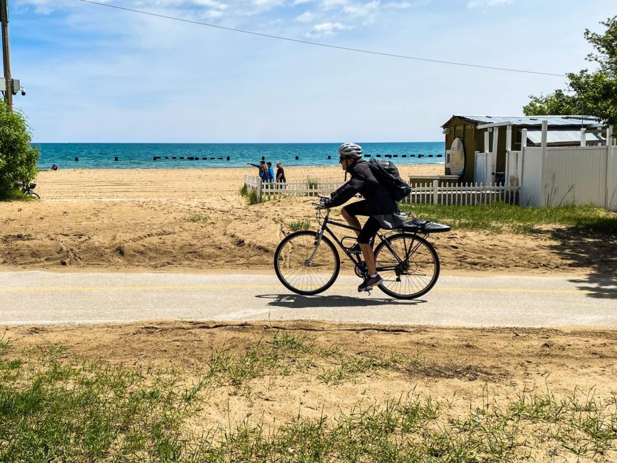 COASTING ALONG. A cyclist bikes by North Avenue Beach, the lake glistening behind them. The 18.5-mile path, which stretches from Edgewater to South Shore, provides spectacular views of the city, an enjoyable form of exercise, and direct access to Chicago’s beaches.   