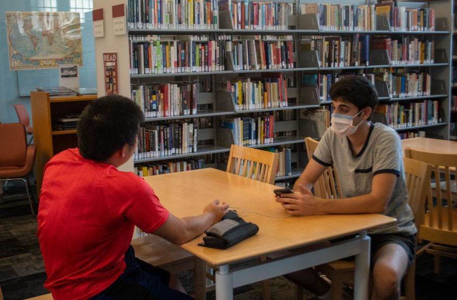 Seniors Ege Halac (masked) and Jeffery Huang (unmasked) talk in the Pritzker-Traubert Family Library. 