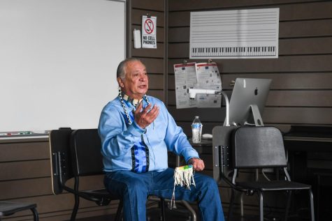 Keith Bear sits in a music classroom and talks to students about his music and storytelling. He crafts flutes and uses them to create musical compositions that tell stories. 