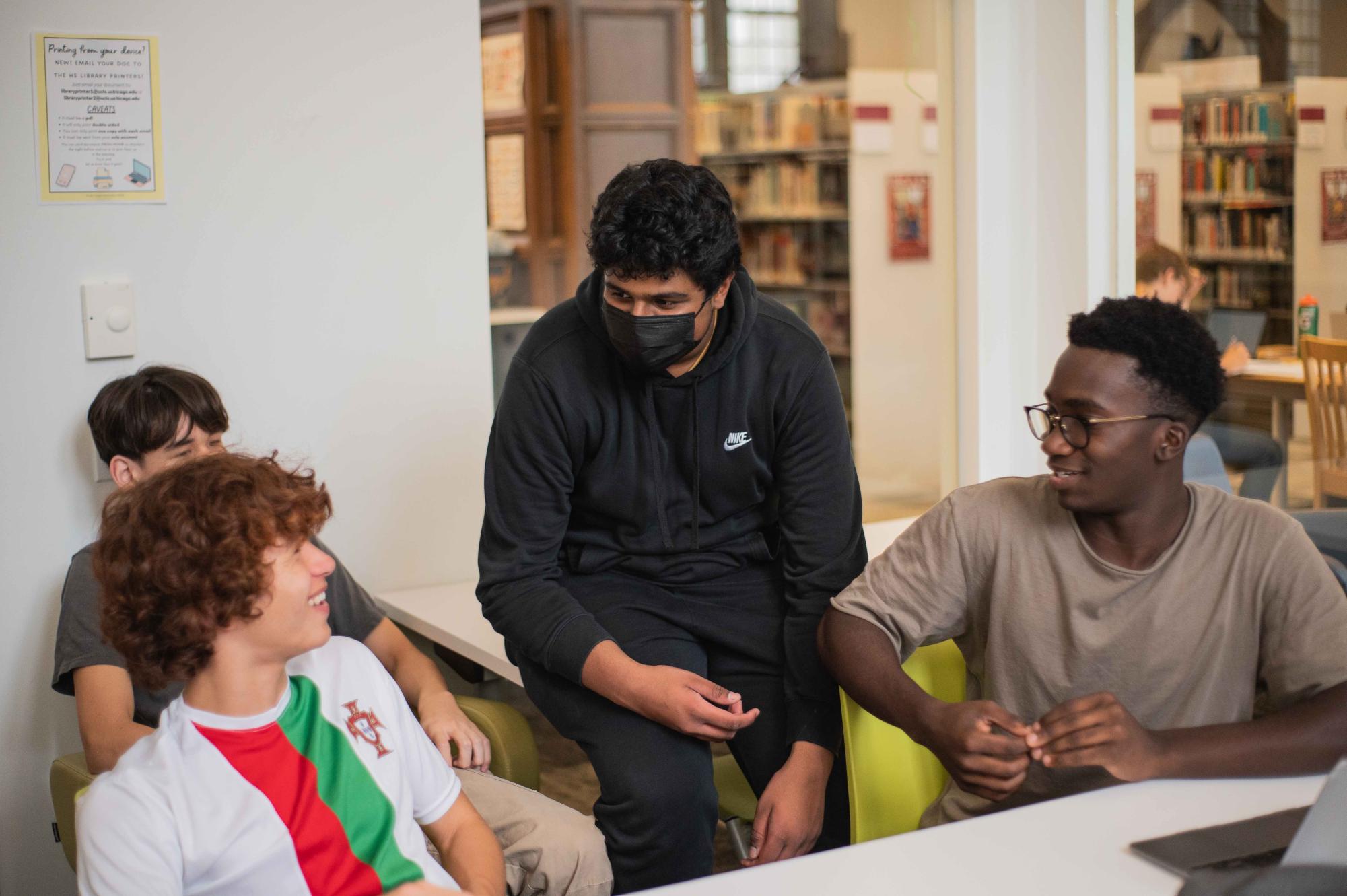 Oliver Go, Ketan Kandula, wearing a mask, and George Ofori-Mante converse in a library room. 