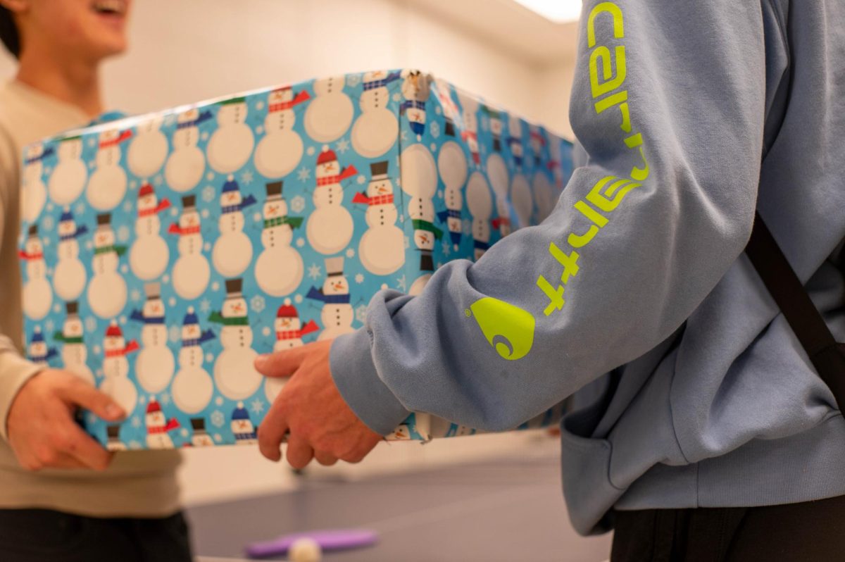 A+student+hands+a+present+covered+in+festive+wrapping+paper+to+another+student.+