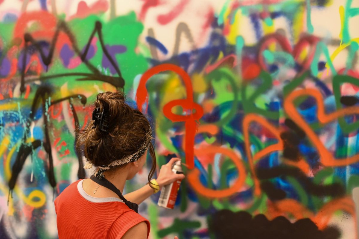 Surrounded by graffiti in the spray painting room on the third floor of Gordon Parks Arts Hall, ninth grader August Nyenhuis adds spray-painted figures to the walls. This workshop allowed people to spray paint the walls of the room and different items of clothing.

