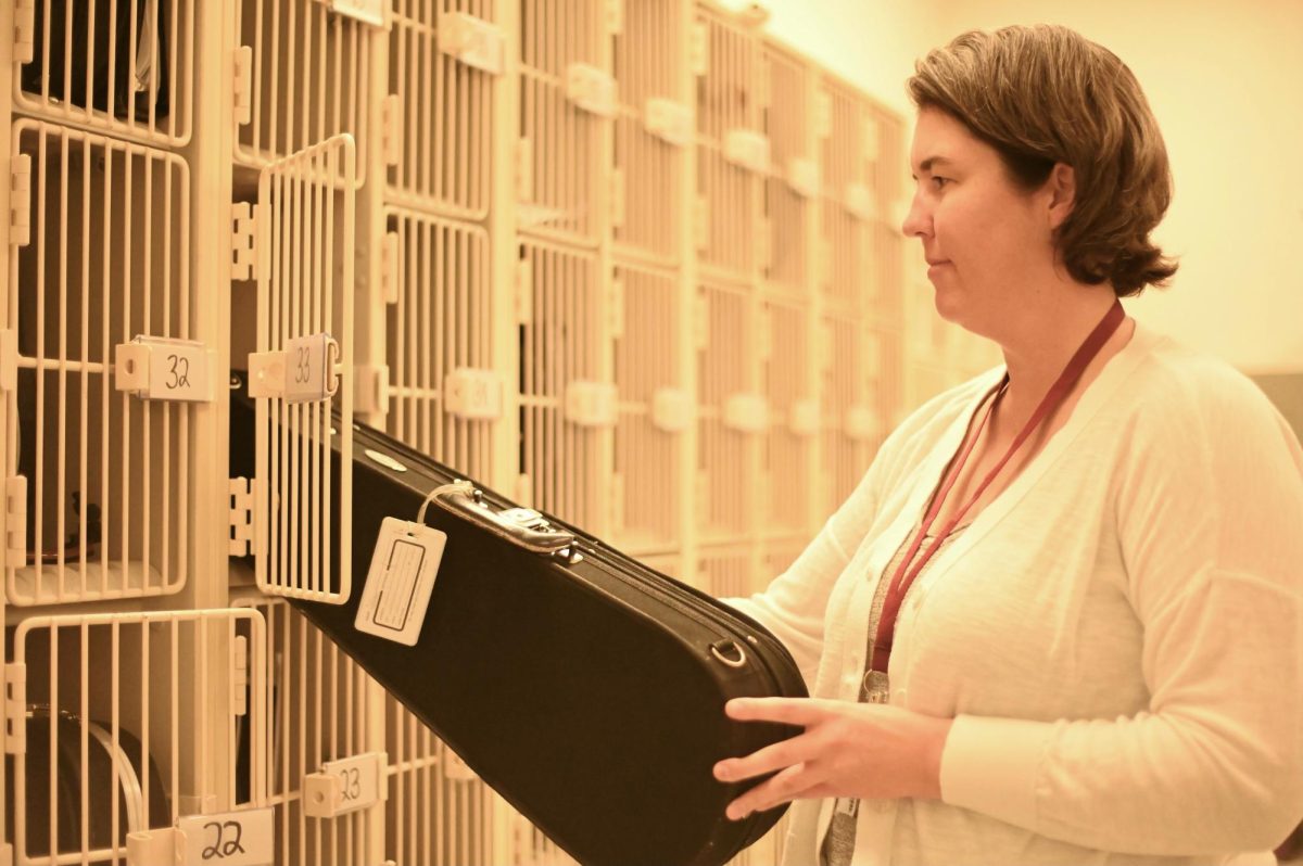 Music teacher Bridget Andes puts an instrument into a locker. Music faculty have been coping with an influx of new work after the removal of an important support role due to budget cuts.