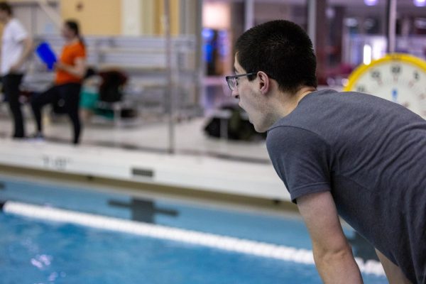 Despite being sidelined due to injuries, Junior Zachary Wong leans over the pool, cheering on his teammates during the boys swimming and diving meet against Latin on Jan. 29.