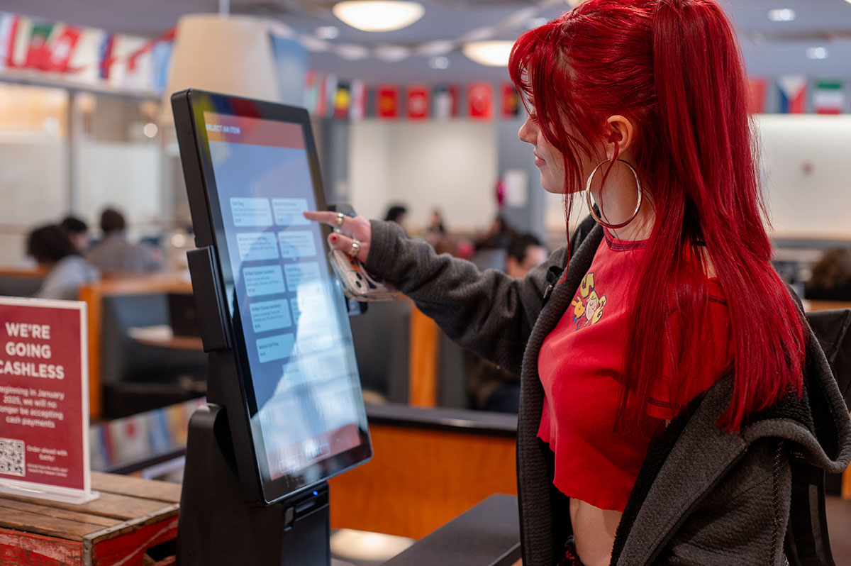 OFF-CAMPUS BITES. Sophomore Laurel Farmer taps on the kiosk to place an order at Everett Kovler Cafe across the street from Lab. Some studies say that open campus policies lead to increased consumption of fast food, but these concerns vary based on individual choices and eating habits.