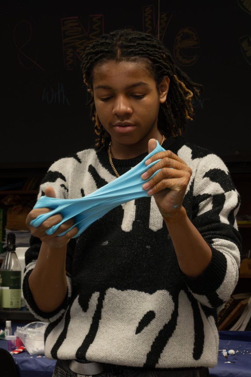 STRETCHED THIN. Sleeves rolled back to avoid dirtying his clothing, sophomore Brandon Coston-Criswell stretches the pale blue slime he made during a workshop. 