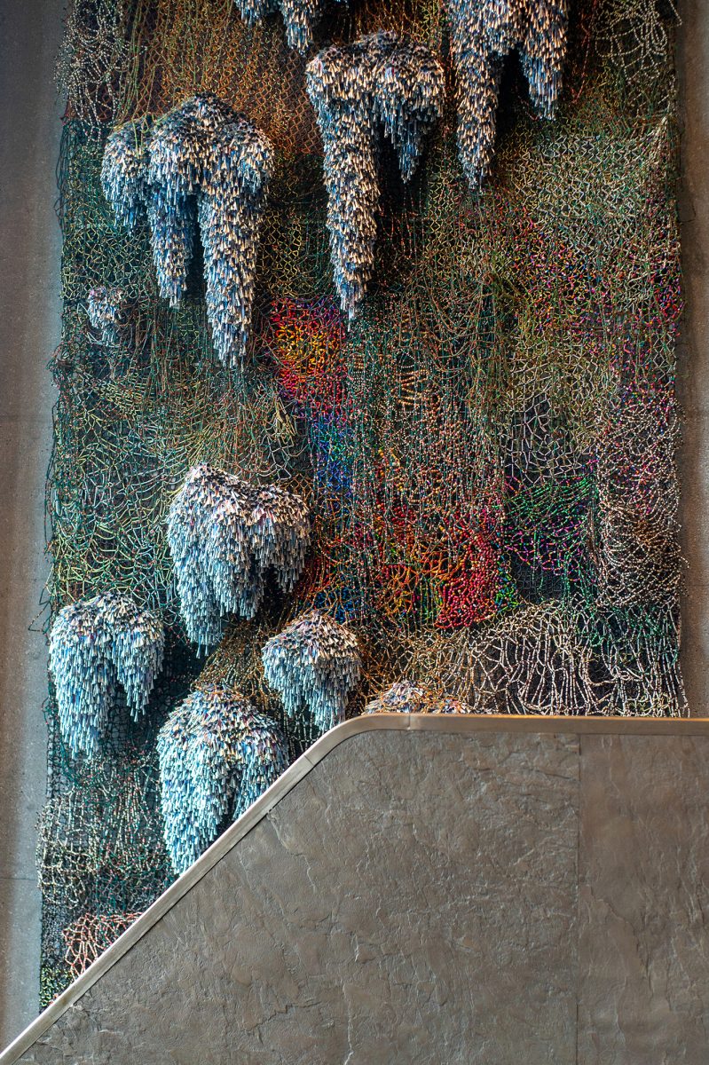 HANGING HANDCRAFT. The 3D art piece” This Land, Shared Sky” by artist Nick Cave stands three stories tall on the west wall of the museum. It includes materials such as beads, nets, and bells. Nick Cave is a Chicago-based sculptor most famous for his Soundsuits, sculptural costumes which use similarly unconventional materials.