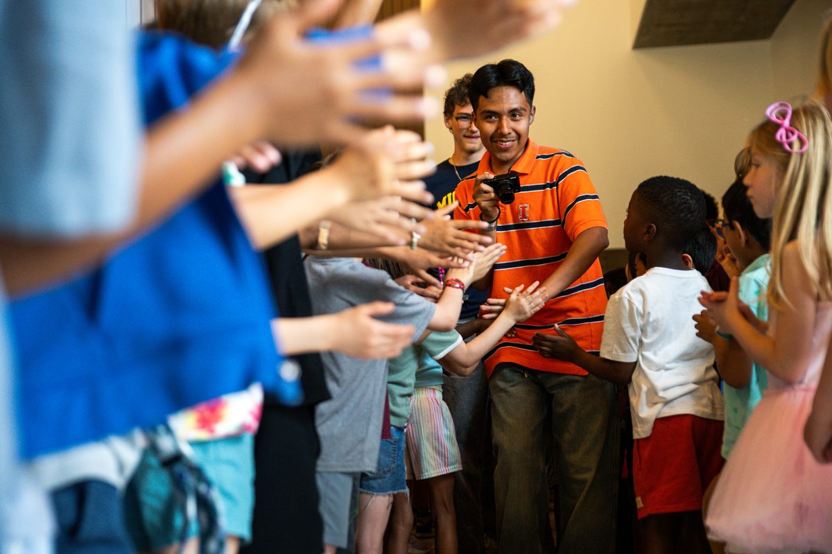INTERGENERATIONAL. Carrying his own camera, senior Osvaldo Carretero high fives younger students as he walks down the hallway during the senior clap-out, which was directly after the assembly on June 4. The annual clap-out took seniors through middle school, lower school and Judd before they returned to outside of the Ken Griffin Auditorium. 